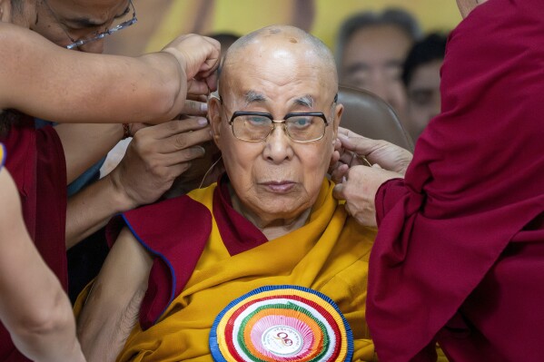 Attendant monks help put a microphone on the spiritual leader of Tibetan Buddhists, the Dalai Lama, during his 90th birthday celebration at the Tsuglakhang temple in Dharamshala, India, Sunday, July 6, 2025.(AP Photo/Ashwini Bhatia)