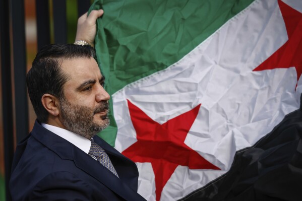 Syria's Foreign Minister Asaad Al-Shibani holds the Syrian Flag during a ceremony where the Syrian flag was added to the 100 flags flying in line at United Nations Headquarters on Friday, April 25, 2025. (AP Photo/Kena Betancur)