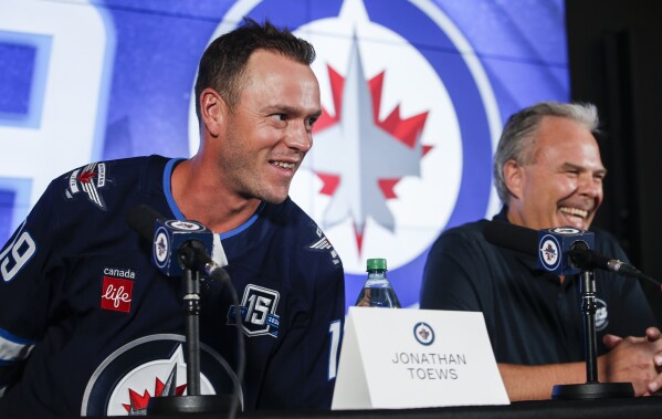 Winnipeg Jets executive vice president and general manager Kevin Cheveldayoff, right, and Jonathan Toews, left, laugh during a news conference held to welcome Toews to the NHL hockey team in Winnipeg, Manitoba, Friday, July 4, 2025. (John Woods/The Canadian Press via AP)