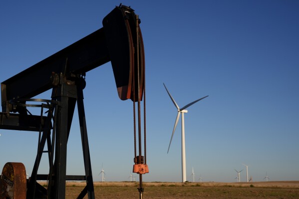 Pumpjacks operate in the foreground while a wind turbines at the Buckeye Wind Energy wind farm rise in the distance Monday, Sept. 30, 2024, near Hays, Kan. (AP Photo/Charlie Riedel, File)