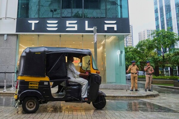 Policemen stand guard as a three-wheeler auto-rickshaw drives past India's first Tesla showroom to be inaugurated in Mumbai, India, Tuesday, July 15, 2025. (AP Photo/Rafiq Maqbool)