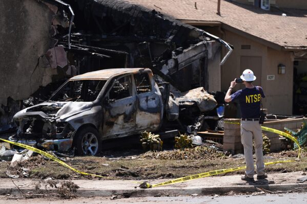 An NTSB worker takes photos of a vehicle and home that were damaged when a small plane crashed into a San Diego neighborhood, setting several homes on fire and forcing evacuations along several blocks early Thursday, May 22, 2025. (AP Photo/Gregory Bull)