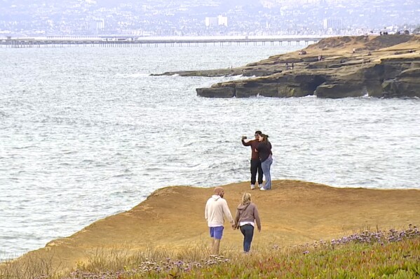 This image taken from video provided by KGTV shows people on a cliff near where a twin-engine Cessna 414 crashed on Sunday, June 8, 2025, leaving a debris field about 3 miles west of Point Loma, a San Diego neighborhood that juts into the Pacific. (KGTV via AP)