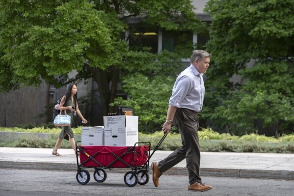 A man pulls a cart with boxes as he walks out of the State Department headquarters, Friday, July 11, 2025, in Washington. (AP Photo/Mark Schiefelbein).