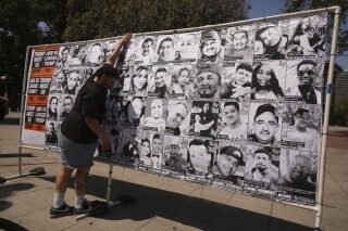 A volunteer sets up an art installation displaying names and faces of people who have been detained, deported, or sent to offshore camps during ICE raids in Southern California, at Olvera Street Plaza in Los Angeles, on Thursday, July 3, 2025. (AP Photo/Damian Dovarganes)