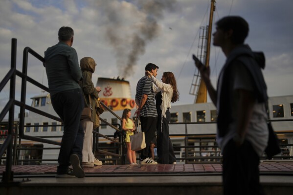 A couple and other passengers wait to board a ferry at the Besiktas terminal on the European side of Istanbul, Turkey, Thursday, May 22, 2025. (AP Photo/Francisco Seco)