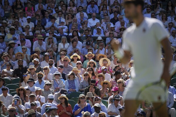 Spectators sit in the sun as they watch Spain's Carlos Alcaraz play Taylor Fritz of the U.S. in a men's singles semifinal at the Wimbledon Tennis Championships in London, Friday, July 11, 2025. (AP Photo/Kin Cheung)