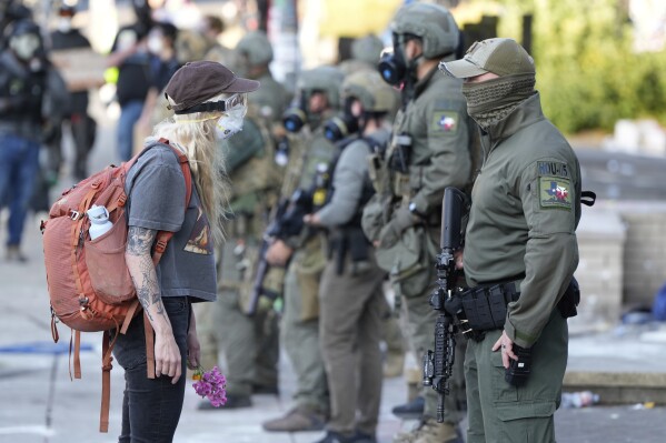 FILE - A woman stands off with a law enforcement officer wearing a Houston Field Office Special Response Team patch outside the U.S. Immigration and Customs building during a protest in Portland, Ore., June 14, 2025. (AP Photo/Jenny Kane, File)