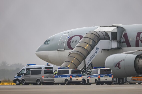 People board a Qatar Airways plane, with federal police vehicles in front of it, on the apron at Leipzig/Halle Airport, Friday, July 18, 2025, Saxony, Schkeuditz. (Jan Woitas/dpa/dpa via AP)