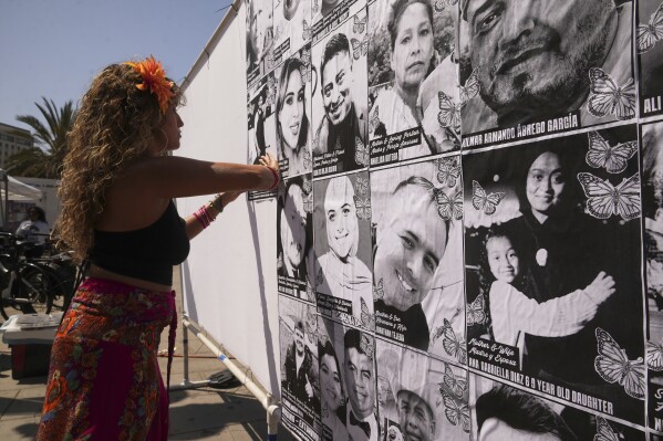 Special needs teacher Deja Nebula sets up an art installation displaying names and faces of people who have been detained, deported, or sent to offshore camps during ICE raids in Southern California, at Olvera Street Plaza in Los Angeles, on Thursday, July 3, 2025. (AP Photo/Damian Dovarganes)