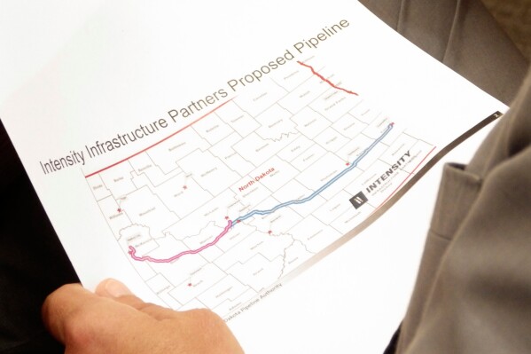 North Dakota Republican Gov. Kelly Armstrong holds a map of a proposed natural gas pipeline on Thursday, June 26, 2025, during a meeting of the Industrial Commission at the state Capitol in Bismarck, N.D. (AP Photo/Jack Dura)