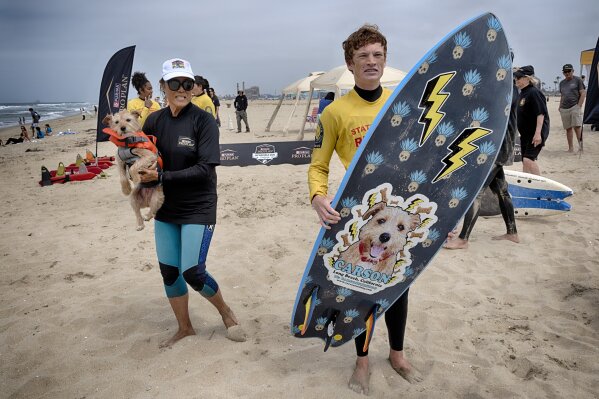 CORRECTION CARSON DID NOT WIN - Carson poses with his coach Jill Nakano, left, and his surfboard during the annual Incredible Dog Challenge western regional surfing competition in Huntington Beach, Calif., Friday, June 20, 2025. (AP Photo/Richard Vogel)
