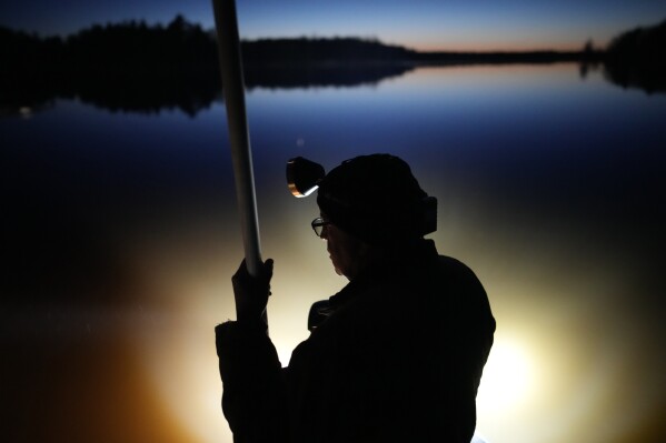 Lights illuminate the water as Mick Tainter holds a spear while fishing at the Chippewa Flowage on the Lac Courte Oreilles Reservation, Sunday, April 14, 2024, near Hayward, Wis. (AP Photo/John Locher)