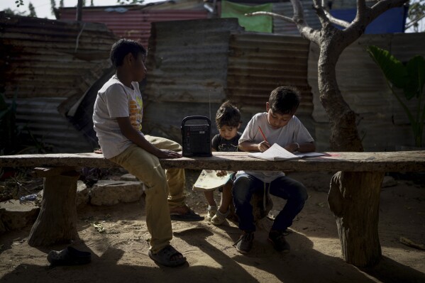 Indigenous children do their homework outside their home in the Villa del Sol neighborhood on the outskirts of Riohacha, Colombia, Tuesday, Feb. 4, 2025. (AP Photo/Ivan Valencia)