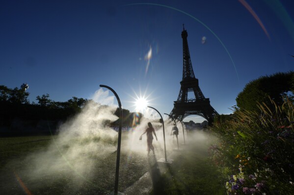 A spectator walks through a water mist sprayer on her way to Eiffel Tower Stadium to watch a beach volleyball at the 2024 Summer Olympics, Sunday, July 28, 2024, in Paris, France. (AP Photo/Robert F. Bukaty)