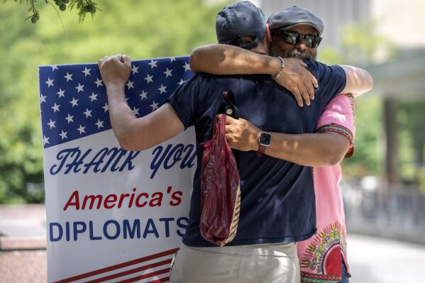 FILE - A man hugs former Foreign Service employee Bob Gilchrist, of Washington, left, as he holds a sign reading "Thank You America's Diplomats" outside the State Department headquarters, July 11, 2025, in Washington. (AP Photo/Mark Schiefelbein, FIle)