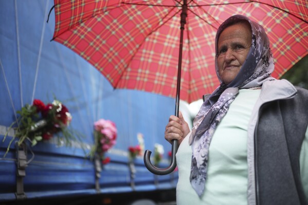 A woman stands next to a truck carrying remains of the identified victims of the 1995 Srebrenica massacre to the Memorial centre in Potocari, where they will be buried on July 11, in Visoko, Bosnia, Wednesday, July 9, 2025. (AP Photo/Armin Durgut)