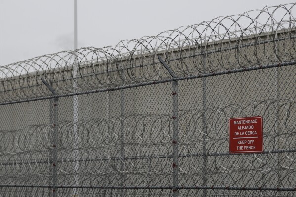 Barbed wire fencing is shown behind a sign in English and Spanish in a recreation yard used by detainees during a media tour of the U.S. Immigration and Customs Enforcement detention center, Dec. 16, 2019, in Tacoma, Wash. (AP Photo/Ted S. Warren, file)
