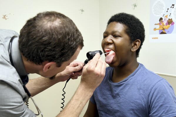 Dr. Joshua Williams, a pediatrician whose federal funding for a vaccine awareness program was cut, examines 12-year-old patient Tiovian Darden in Denver on Tuesday, March 18, 2025. (AP Photo/Thomas Peipert)