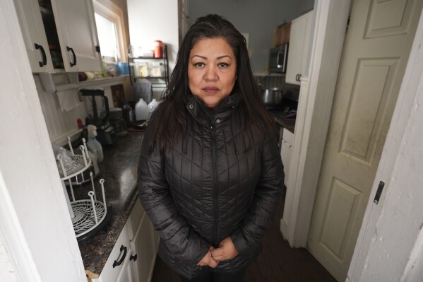 Claudia Ortiz stands in her home with wearing a coat Wednesday, Feb. 19, 2025 after a recent water main break caused flooding in Detroit. (AP Photo/Paul Sancya)