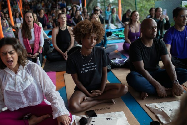 A woman sitting in the lotus position wears a shirt that reads in Portuguese, "Be strong like a mother from the outskirts" while meditating during a Transformation Project yoga class in the Rocinha favela, in Rio de Janeiro, Wednesday, July 9, 2025. (AP Photo/Bruna Prado)