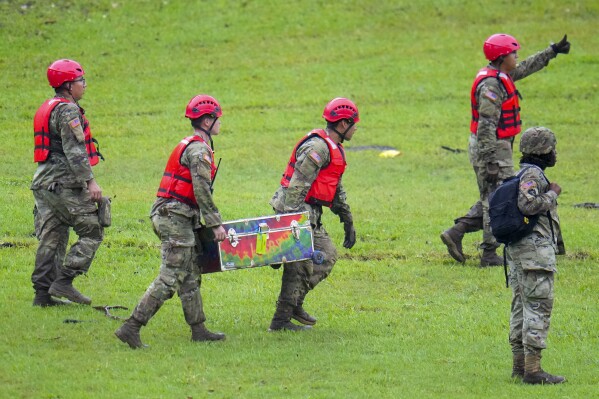 Military personnel carry a camp trunk salvaged down river from Camp Mystic along the Guadalupe River, Sunday, July 6, 2025, in Hunt, Texas, after a flash flood swept through the area. (AP Photo/Julio Cortez)