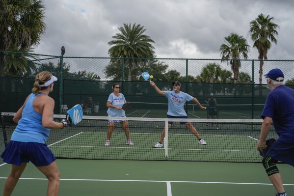 Wearing matching Harris-Walz T-shirts, Glen Smith, 62, and his wife Suzi, 64, play pickleball with other members of The Villages Democratic Club, in The Villages, Fla., Sunday, Sept. 15, 2024. The Smiths say that friends questioned why they would choose to move to such a conservative enclave. "Somebody has to infiltrate," joked Suzi. "Most of our best friends are conservative." Adds Glen, "We know they are red, and they know we are blue, and we all just don't talk about it." (AP Photo/Rebecca Blackwell)
