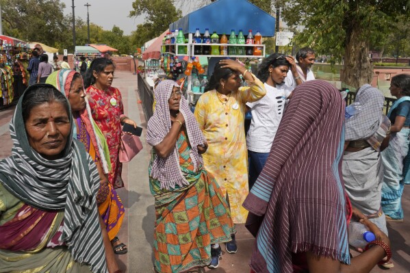 Local tourists cover their heads to shield from the heat as they buy drinking water bottles, in New Delhi, India, Tuesday, June 18, 2024. A monthslong heat wave across swathes of India has killed more than 100 people and led to over 40,000 suspected cases of heat stroke in the last three and a half months, a Health Ministry official said Thursday. (AP Photo/Manish Swarup)