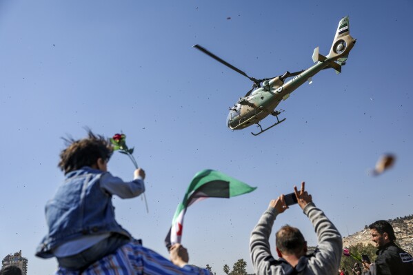 A Syrian army helicopter throws flowers and confetti on a group of demonstrators marking the 14th anniversary of the start of the uprising against Bashar Assad's regime in March 2011, in Umayyad square, Damascus, Syria, Saturday, March 15, 2025. (AP Photo/Ghaith Alsayed)