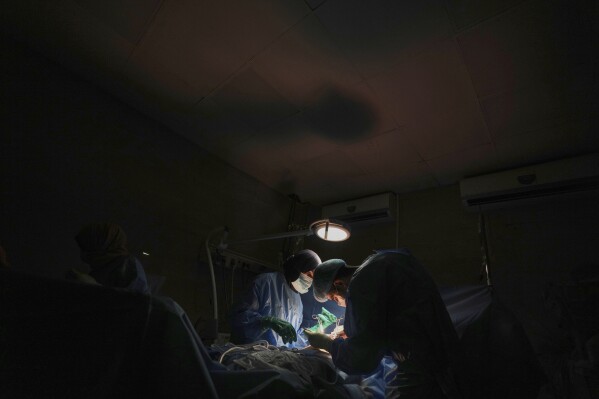 Dr. Abeer Al-Gharbawi, left, performs surgery under the illumination of a battery-powered light during a power outage at Shifa Hospital in Gaza City, Friday, July 4, 2025. (AP Photo/Jehad Alshrafi)