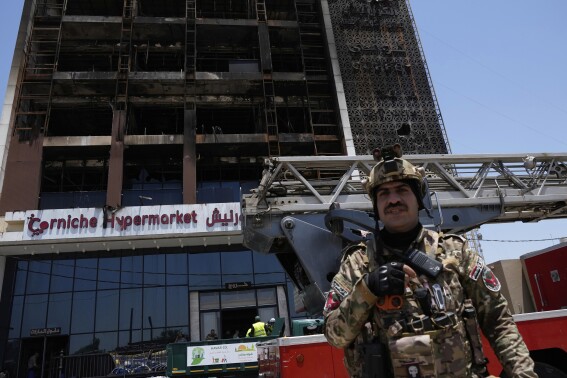 An Iraqi security guard stands in front of a burning hypermarket building in Kut, Iraq, Thursday, July 17, 2025. (AP Photo/Hadi Mizban)