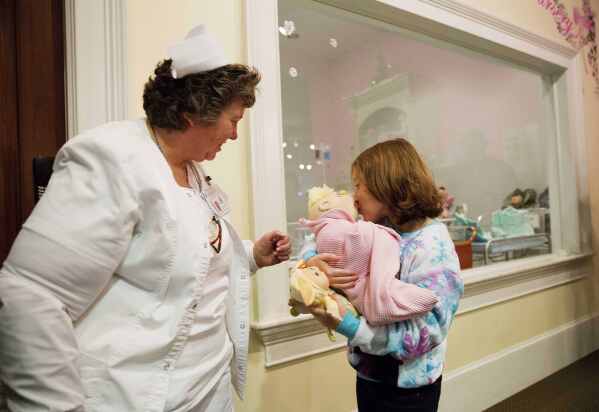 Talon Shaffer, right, kisses a Cabbage Patch Kid after it was delivered by Cyndi Pappadouplos, a "licensed patch nurse" at Babyland General Hospital, the birthplace of Cabbage Patch Kids, in Cleveland, Ga., on Nov. 21, 2014. (AP Photo/David Goldman, File)