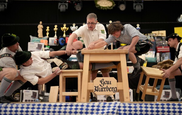 Men dressed in traditional clothes try to pull the opponent over the table at the German Championships in Fingerhakeln or finger wrestling, in Bernbeuren, Germany, Sunday, May 12, 2024. (AP Photo/Matthias Schrader)