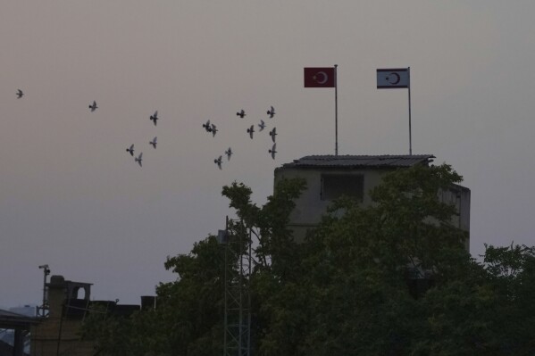 Birds fly behind a Turkish military guard post with a Turkish, left, and Turkish Cypriot breakaway flags next of a U.N buffer zone in divided capital Nicosia, Cyprus, Thursday, July 17, 2025. (AP Photo/Petros Karadjias)