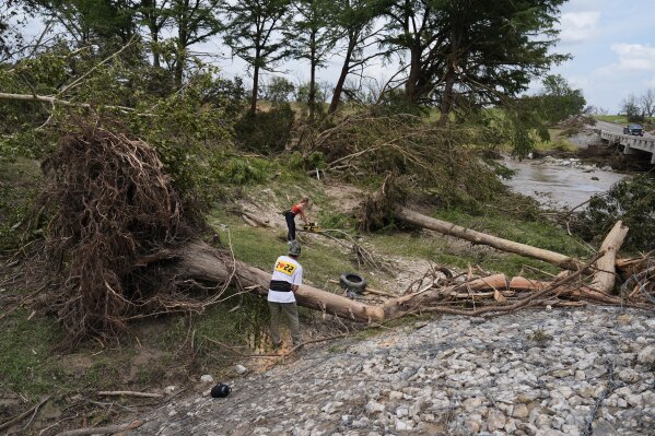 Hayley Bosworth, back, and Simon Ball, foreground, cut tree branches during clean-up efforts after flooding in Center Point, Texas, Monday, July 7, 2025. (AP Photo/Ashley Landis)