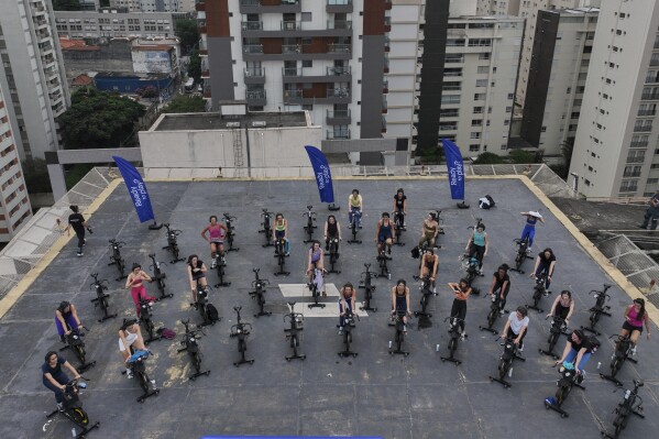 Women attend a spinning class on a hotel building's helipad in Sao Paulo, Tuesday, March 18, 2025. (AP Photo/Andre Penner)