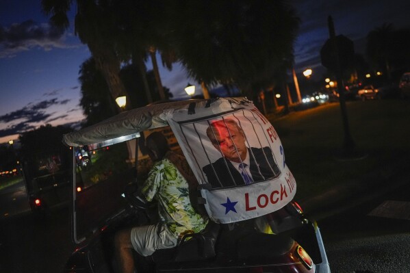 A supporter of Democratic presidential candidate Vice President Kamala Harris drives a golf cart with a banner reading "Trump for Prison" and an image of Republican presidential nominee former President Donald Trump behind bars, as he participates in a parade of decorated golf carts following a Harris campaign event with second gentleman Doug Emhoff, in The Villages, Fla., Friday, Sept. 13, 2024. (AP Photo/Rebecca Blackwell)