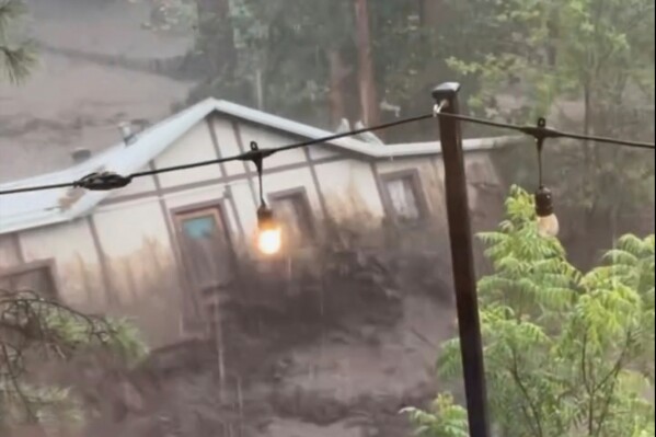 In this image taken from video, a house is carried away by flash flooding behind a house in Ruidoso, N.M., Tuesday, July 8, 2025. (Kaitlyn Carpenter via AP)