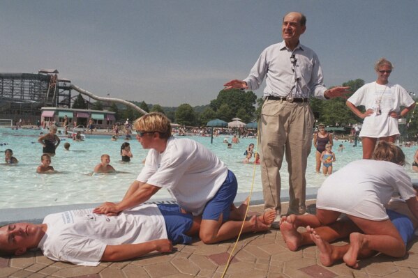 Dr. Henry J. Heimlich uses lifegaurds at Coney Island swimming pool in suburban Cincinnati on Friday, July 9, 1999, to demonstrate how the Heimlich maneuver can help save people from drowning. (AP Photo/Tony Tribble, File)