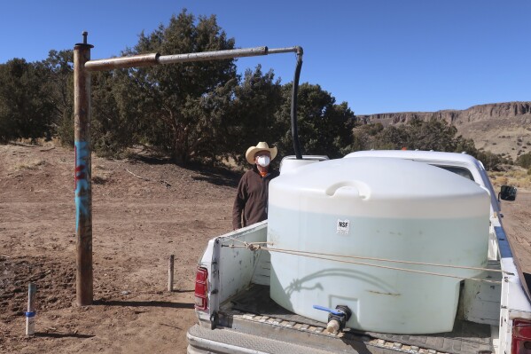 Phillip Yazzie espera que un tanque de agua en la parte trasera de su camioneta pickup sea llenado en Teesto, Arizona, en la Navajo Nation, el 11 de febrero de 2021. (AP Foto/Felicia Fonseca, archivo)